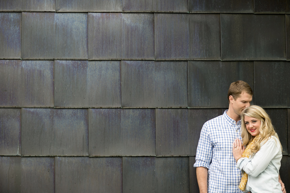 A man and woman stand close together in front of a dark tile wall; the man looks down while the woman faces forward, smiling. Jessica Hill Photography - Wedding Photographer - Oregon