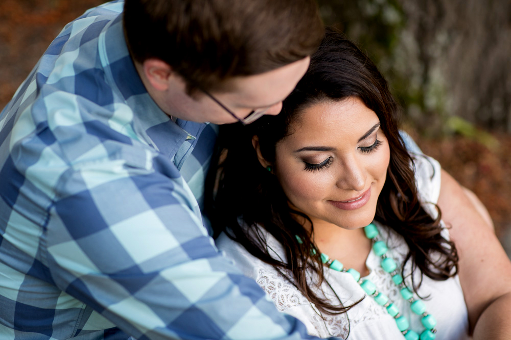 A man in a blue plaid shirt embraces a woman wearing a white blouse and turquoise necklace, both seated and looking down. Jessica Hill Photography - Wedding Photographer - Oregon