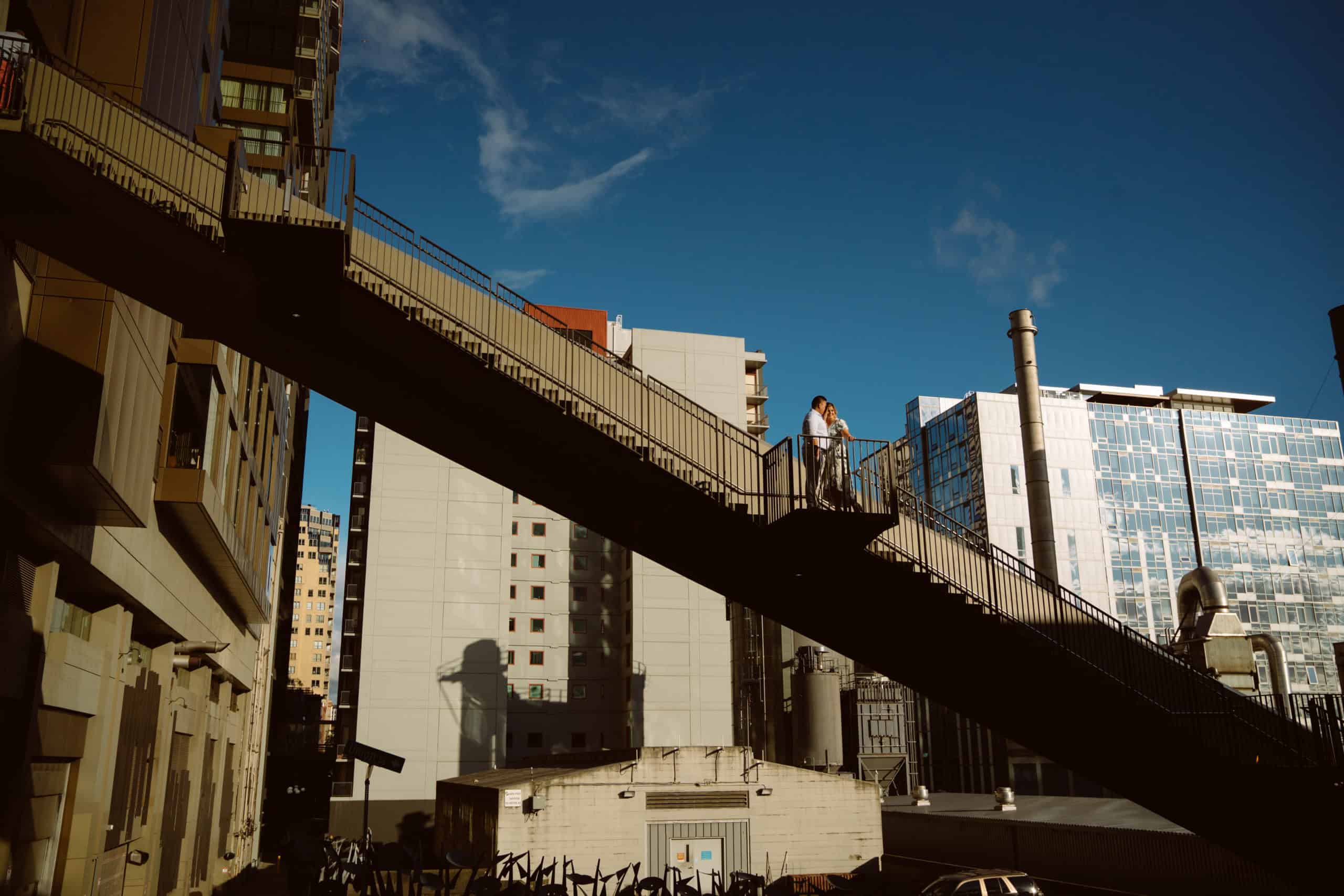 Couple on city pedestrian bridge overlooking skyscrapers.