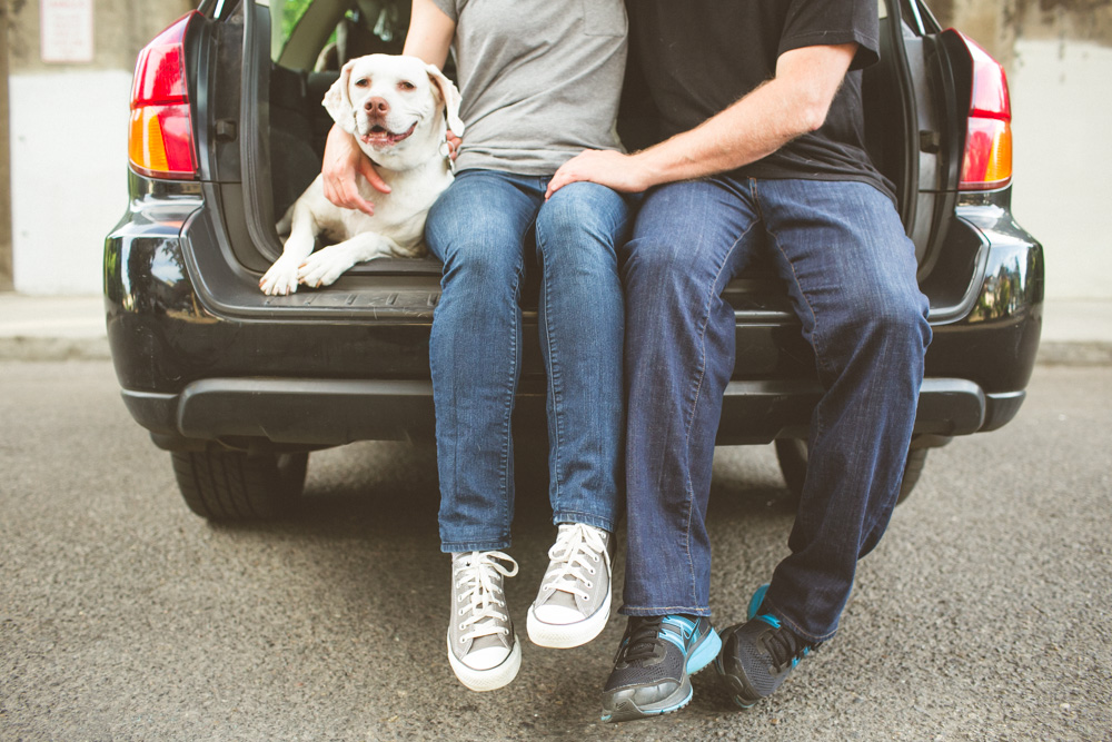 Two people sit on the open trunk of a car with a white dog beside them, all facing forward. The scene appears casual and relaxed. Jessica Hill Photography - Wedding Photographer - Oregon