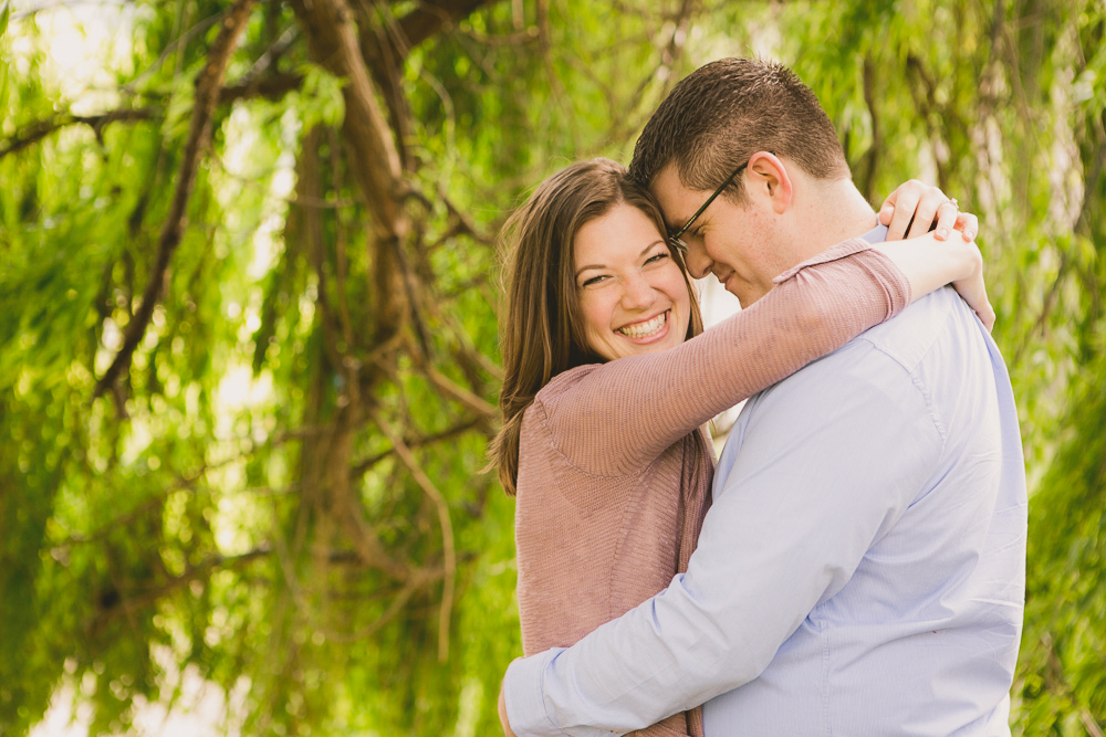 A woman and a man embrace and smile outdoors in front of green, leafy trees. Jessica Hill Photography - Wedding Photographer - Oregon