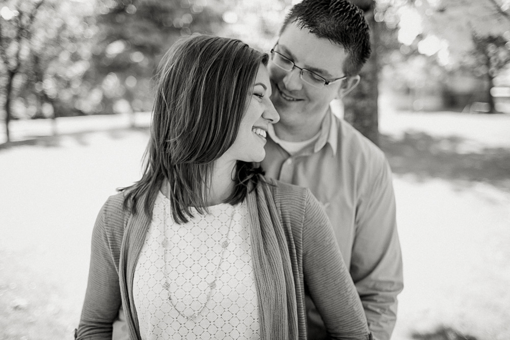 A couple stands close together outside, smiling and looking at each other, with trees and sunlight in the background. Jessica Hill Photography - Wedding Photographer - Oregon