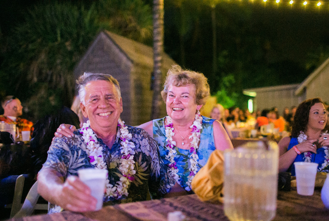 A bride and groom embrace on rocky shore at sunset, with waves crashing behind them and a dramatic sky overhead, blending shades of purple, pink, and blue as evening falls over the ocean. Jessica Hill Photography - Wedding Photographer - Oregon