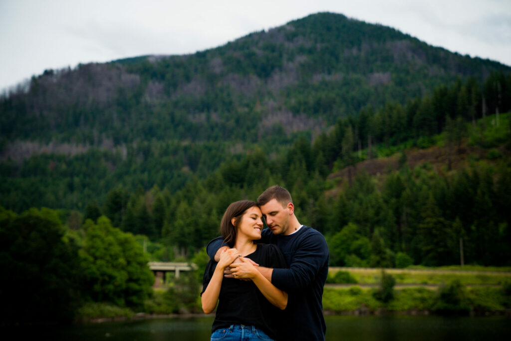 Couple embracing with mountain and forest background.