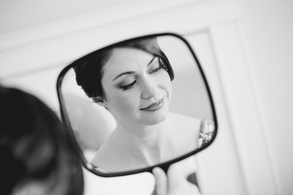 A woman’s face is reflected in a handheld mirror as she looks down and smiles slightly; the image is in black and white. Jessica Hill Photography - Wedding Photographer - Oregon