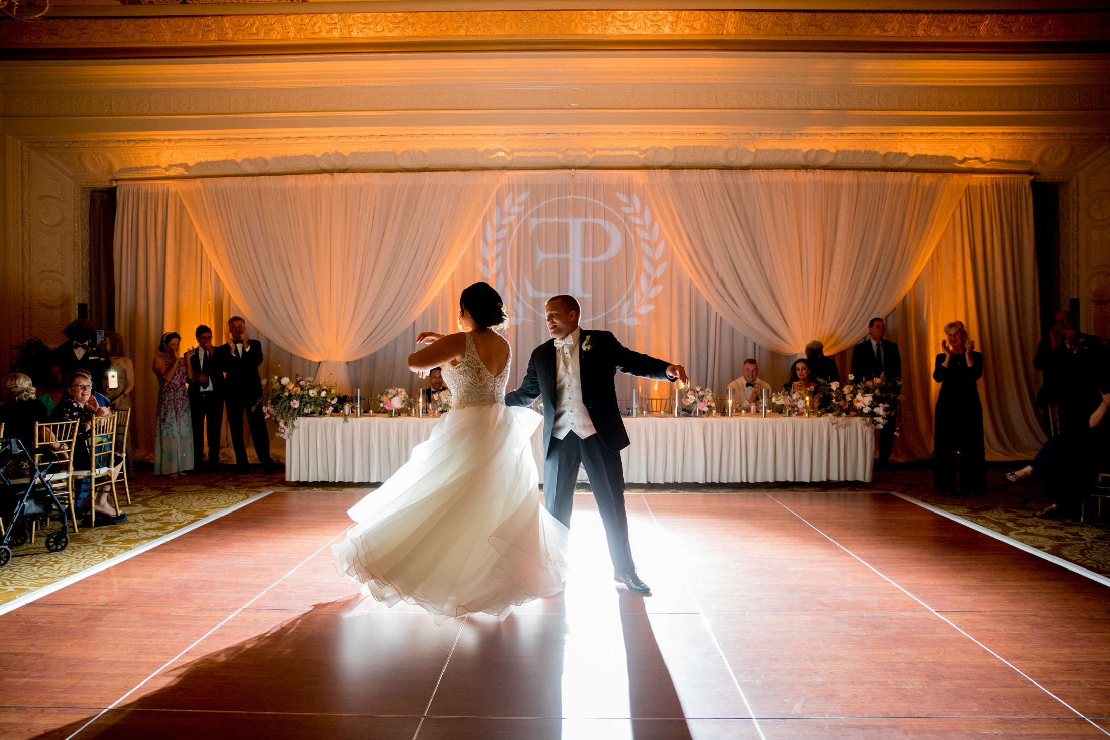 A bride and groom dance together on a ballroom floor as guests watch from their seats at a formal wedding reception. Jessica Hill Photography