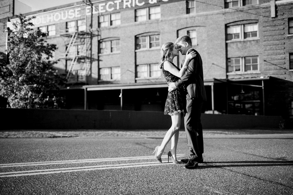 A woman in a black lace dress and blue heels stands arm-in-arm with a man in a black suit and tie on a city sidewalk. Jessica Hill Photography - Wedding Photographer - Oregon