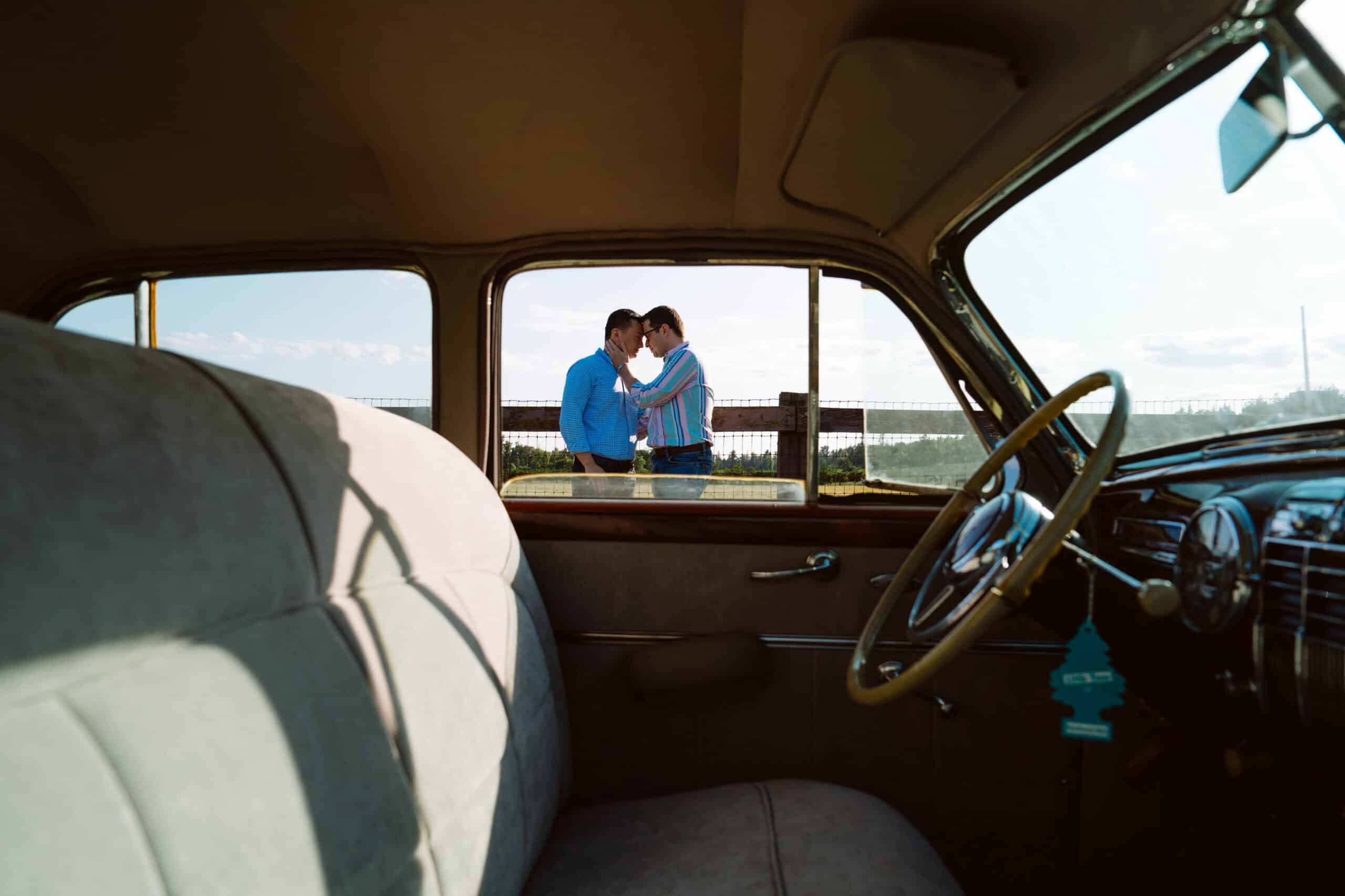 Couple standing by classic car, touching foreheads.