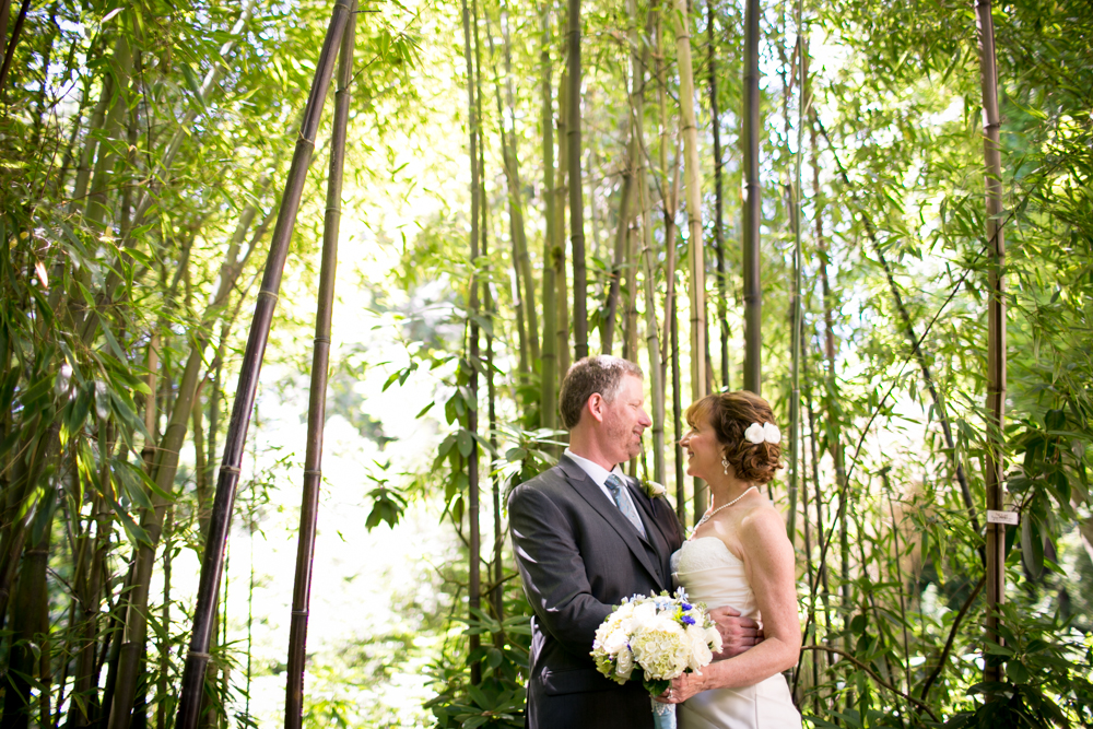 A bride and groom stand facing each other and smiling in a bamboo forest, with the bride holding a bouquet of flowers. Jessica Hill Photography - Wedding Photographer - Oregon