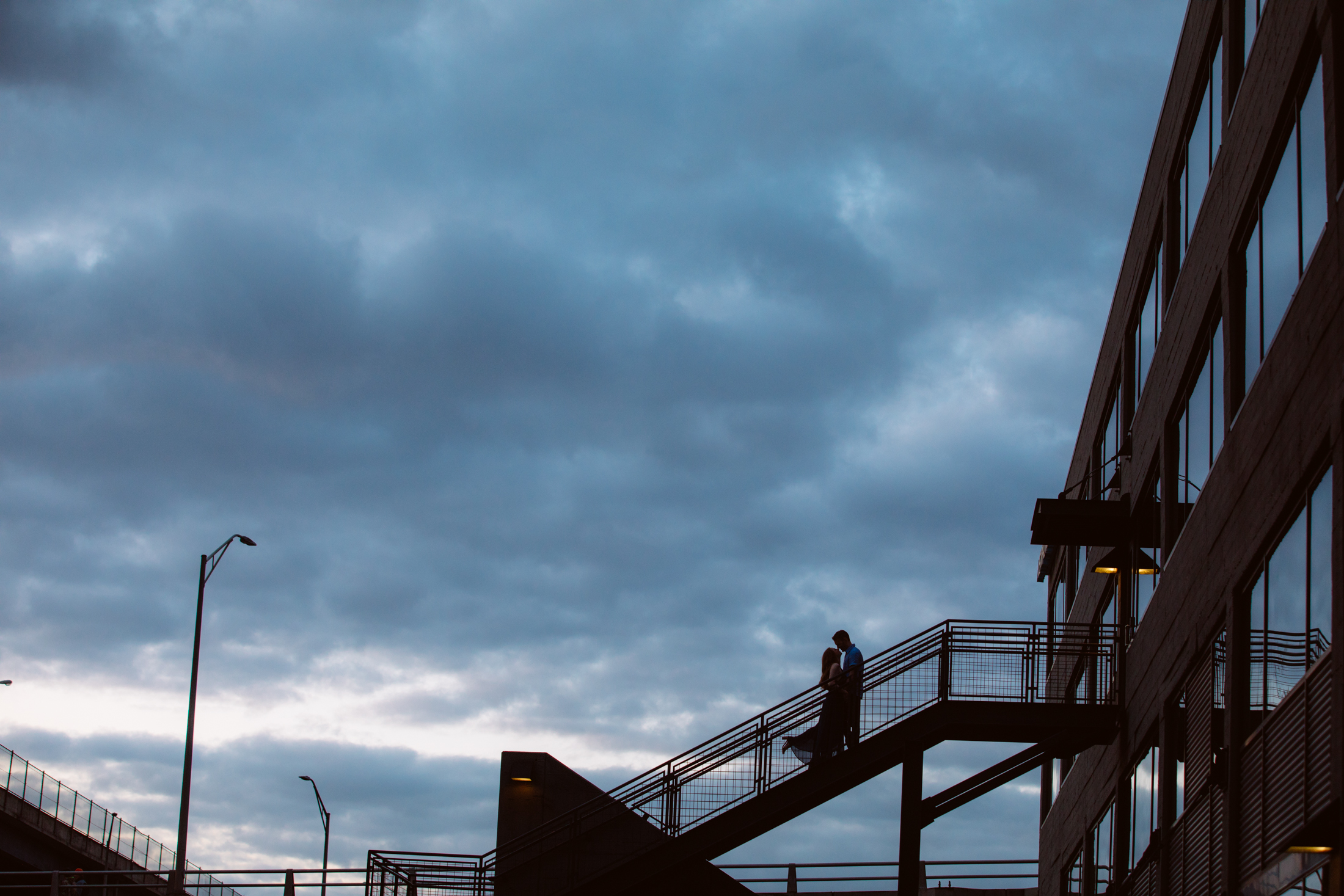 Two people walk up an outdoor staircase attached to a modern building under a cloudy evening sky. Jessica Hill Photography