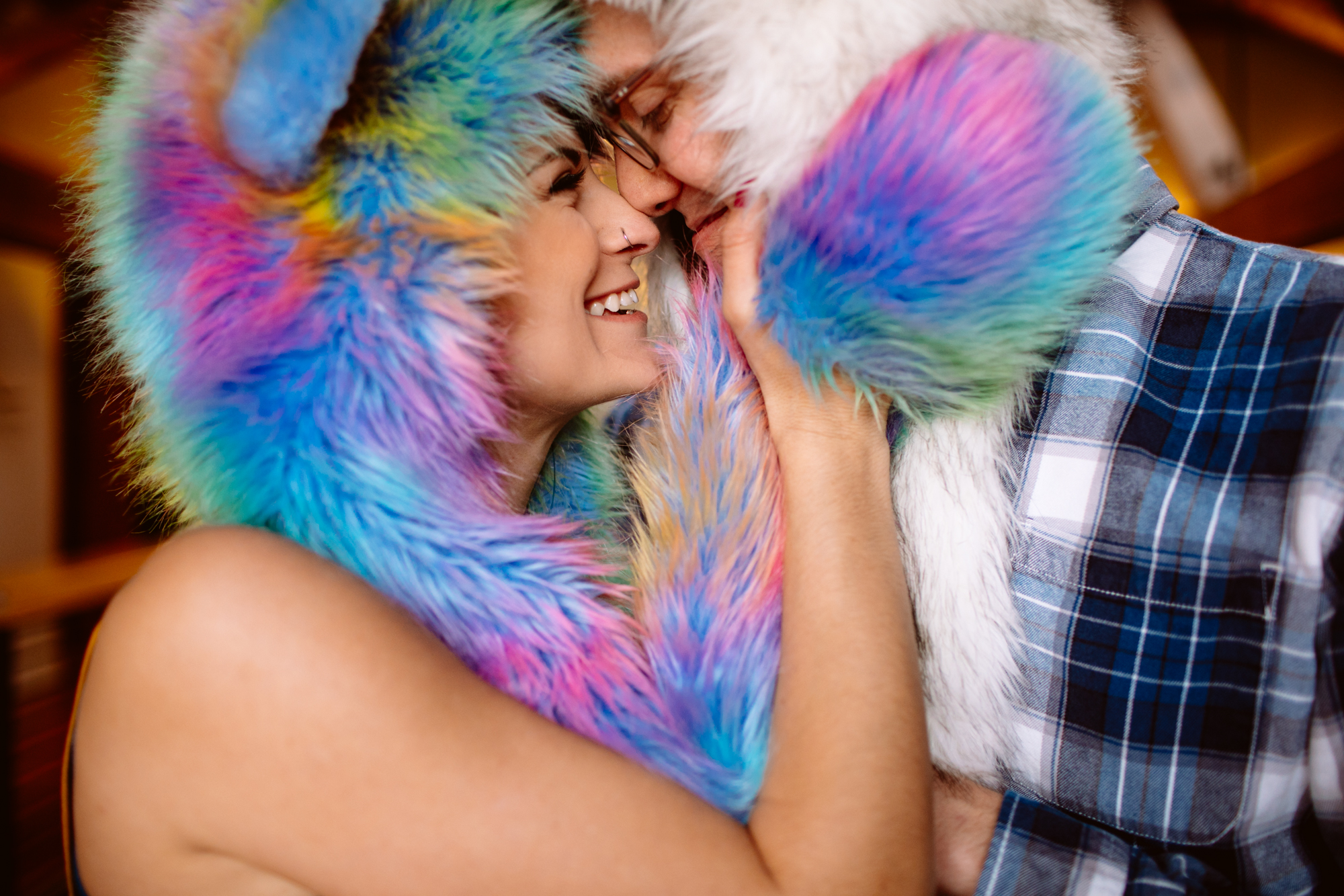 Two people wearing colorful, furry hooded garments touch faces and smile closely at each other indoors. Jessica Hill Photography
