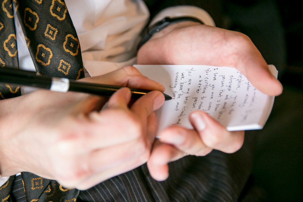 A person in business attire writes notes with a pen on a small notepad, holding it in their hand. The text on the notepad is partially visible but not fully readable. Jessica Hill Photography - Wedding Photographer - Oregon