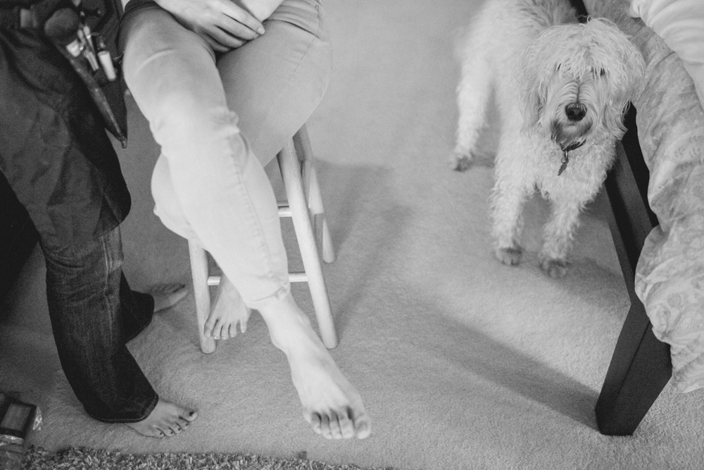 A person sits barefoot on a stool next to another standing person, while a fluffy dog stands on a carpeted floor nearby. Jessica Hill Photography - Wedding Photographer - Oregon