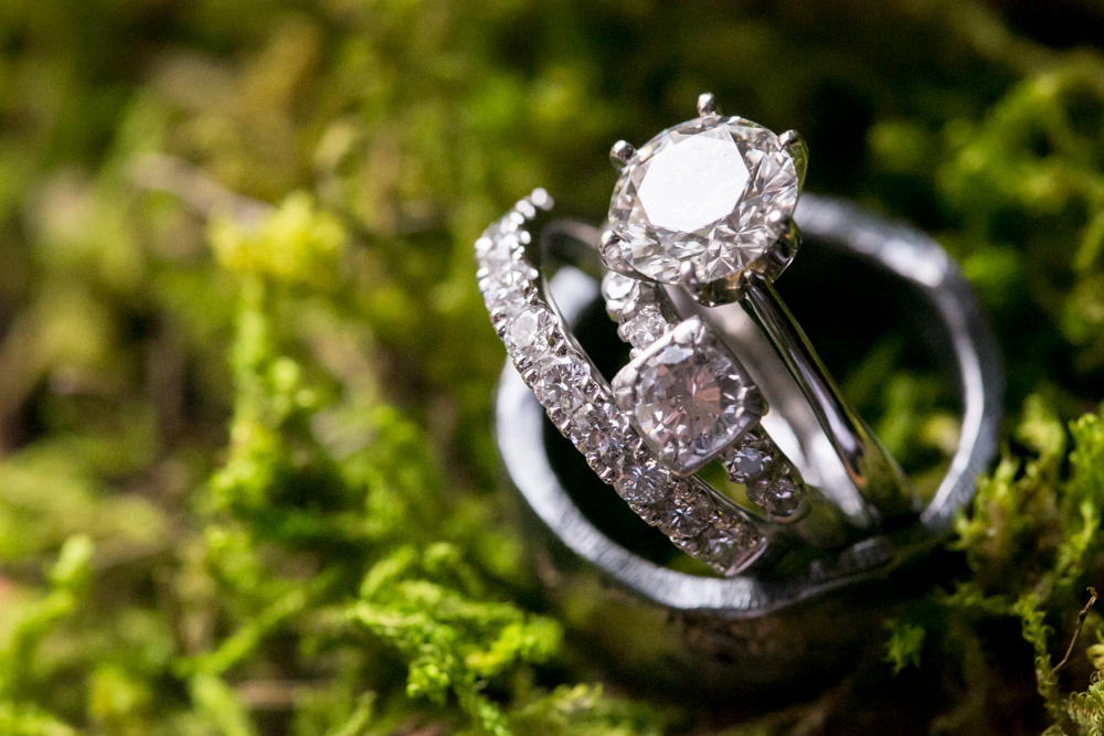 Close-up of three diamond rings, including an engagement ring and wedding bands, placed on a bed of green moss. Jessica Hill Photography - Wedding Photographer - Oregon