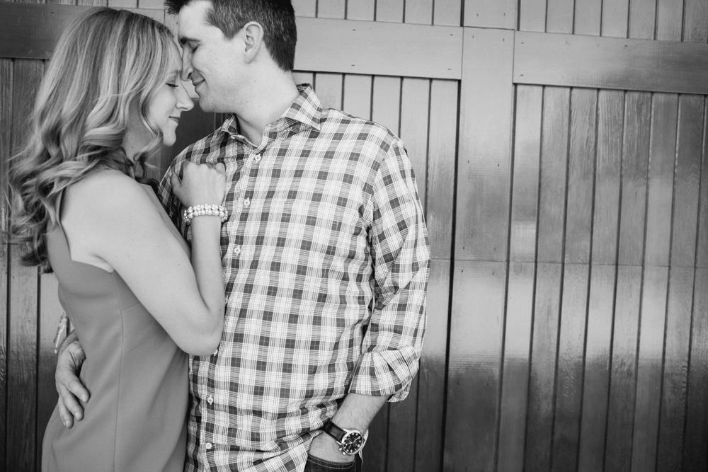 A woman and a man stand close together, smiling, with their foreheads touching in front of a wooden wall. Jessica Hill Photography - Wedding Photographer - Oregon