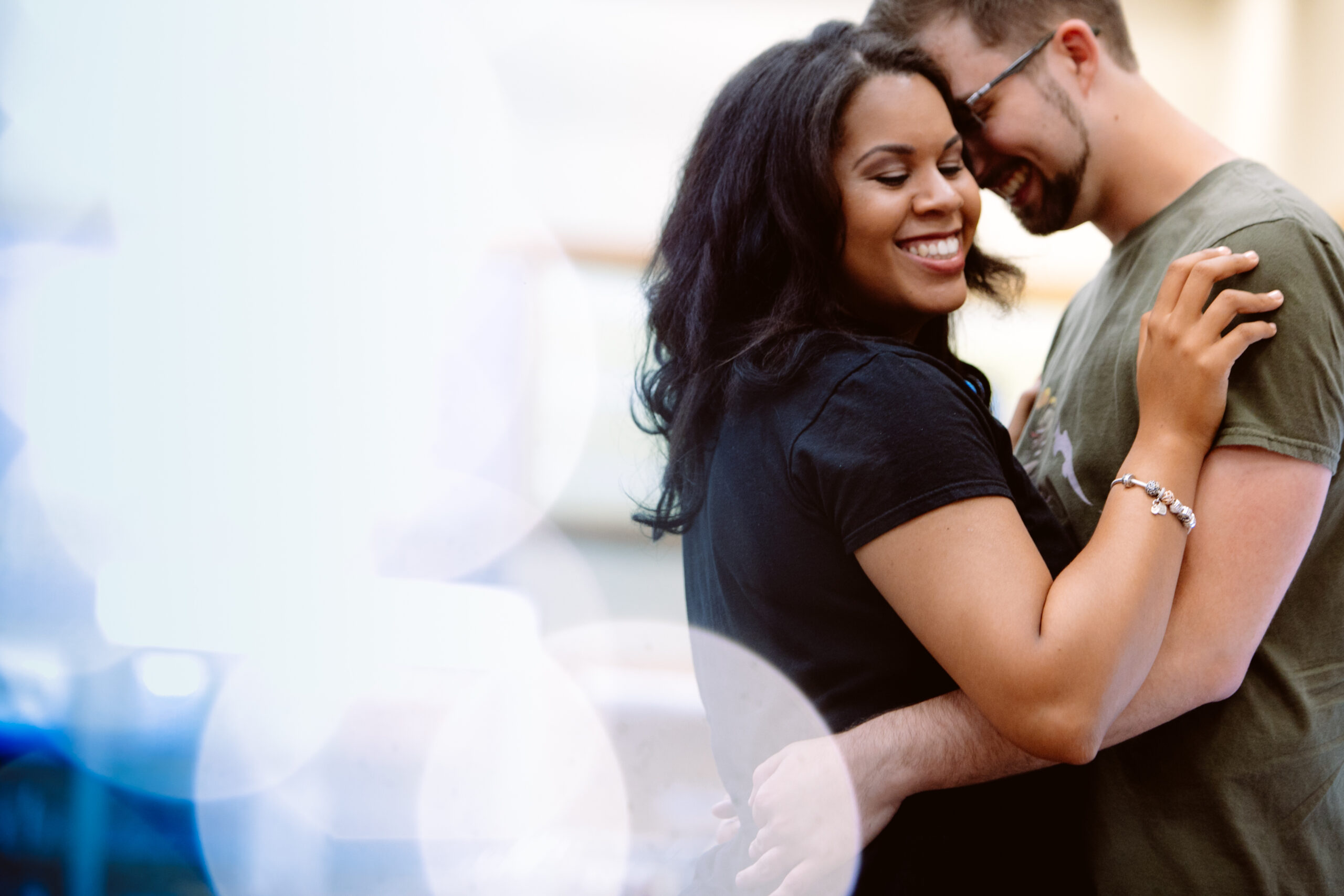 A woman and a man stand close together, smiling and embracing each other, with a soft, out-of-focus background. Jessica Hill Photography