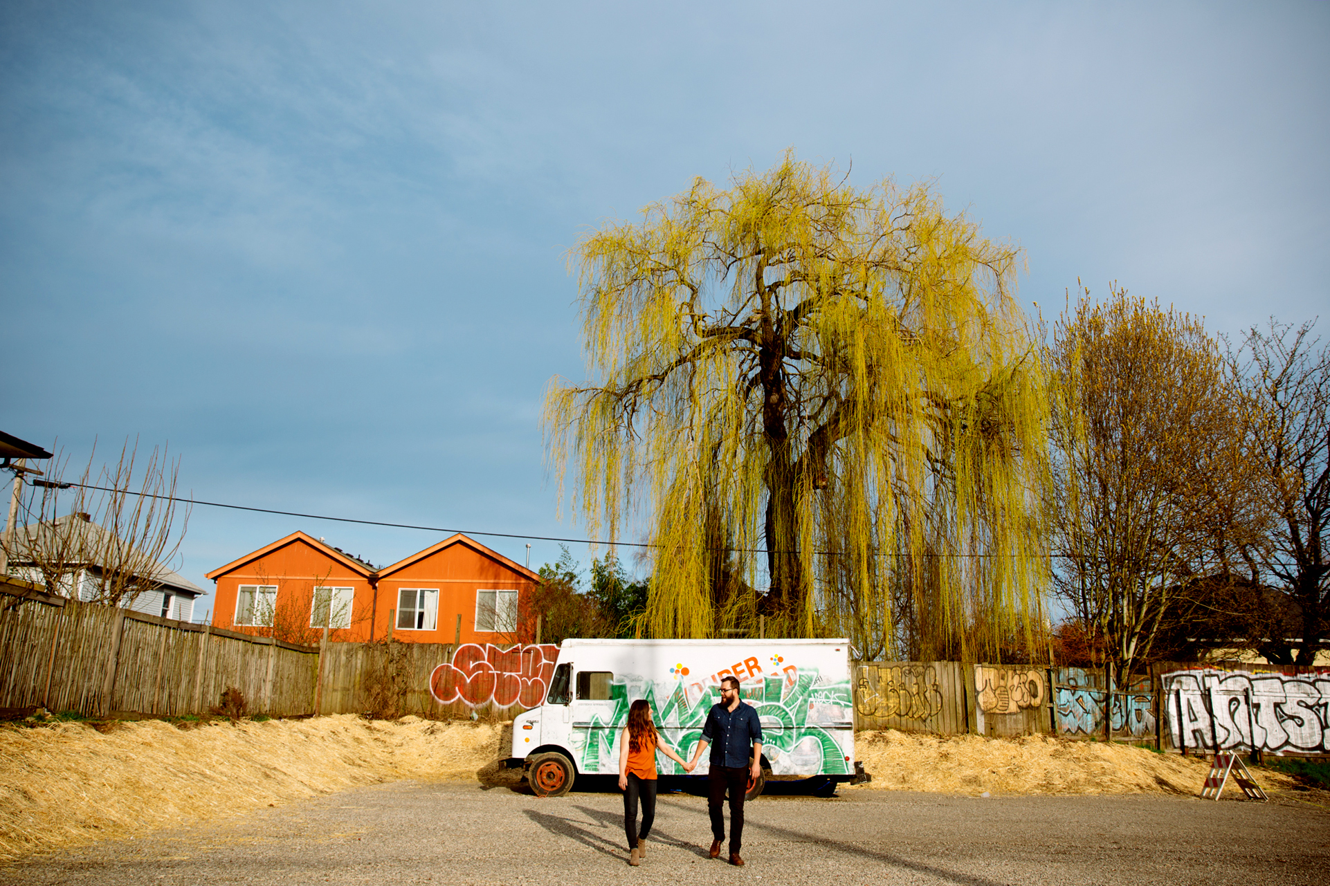 An elegantly dressed woman and man clink wine glasses at an outdoor event, sitting by a table with a large floral centerpiece. String lights and trees create a festive evening atmosphere in the background. Jessica Hill Photography - Wedding Photographer - Oregon