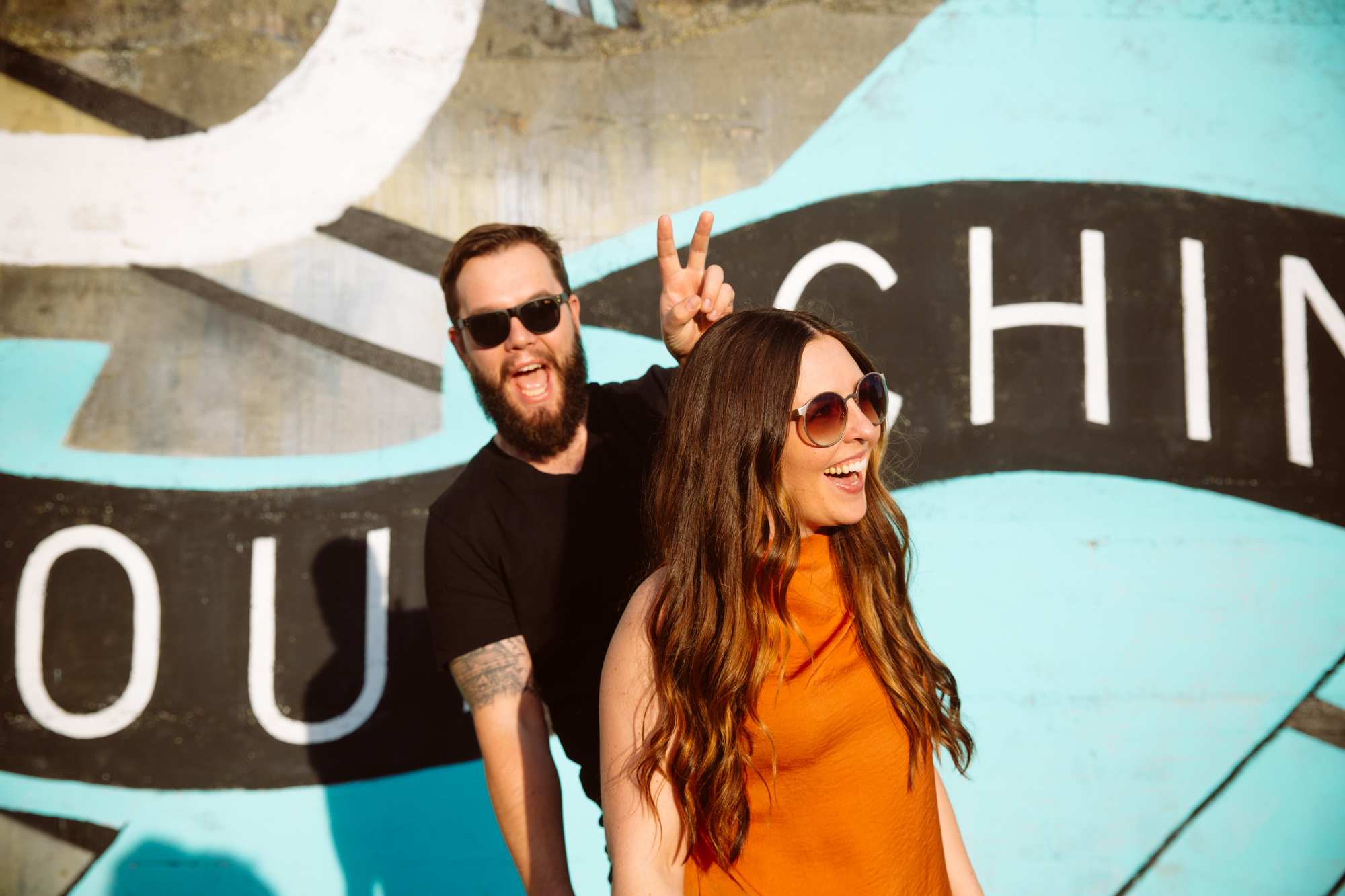 A smiling bride in a strapless white wedding gown is helped by two bridesmaids in sparkly dresses as she gets ready. Bright light streams through large windows behind them. Jessica Hill Photography - Wedding Photographer - Oregon