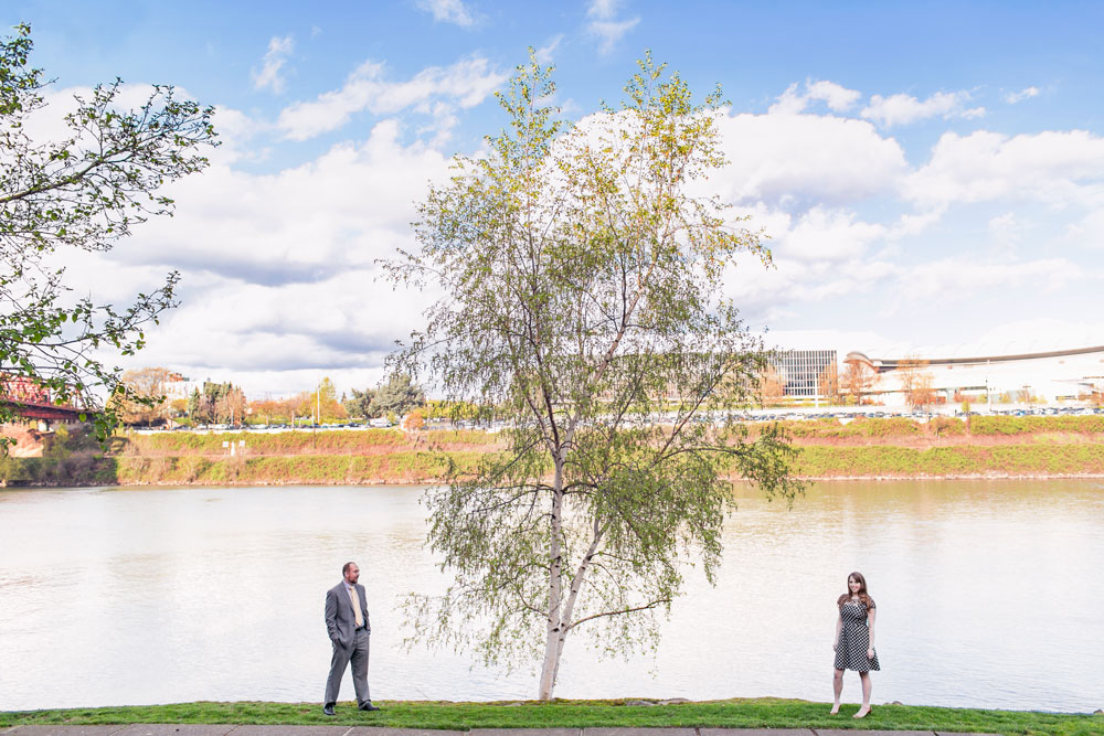 A man in a gray suit and a woman in a polka dot dress with red heels walk hand in hand on a wooden boardwalk by the water. Jessica Hill Photography - Wedding Photographer - Oregon