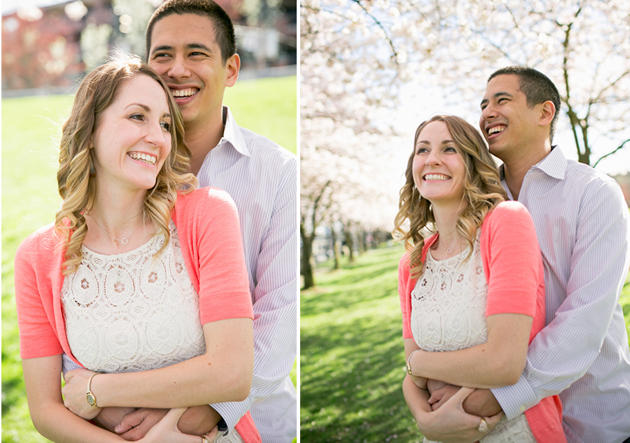 A couple stands outdoors, smiling and embracing, with green grass and blooming trees in the background. Jessica Hill Photography - Wedding Photographer - Oregon