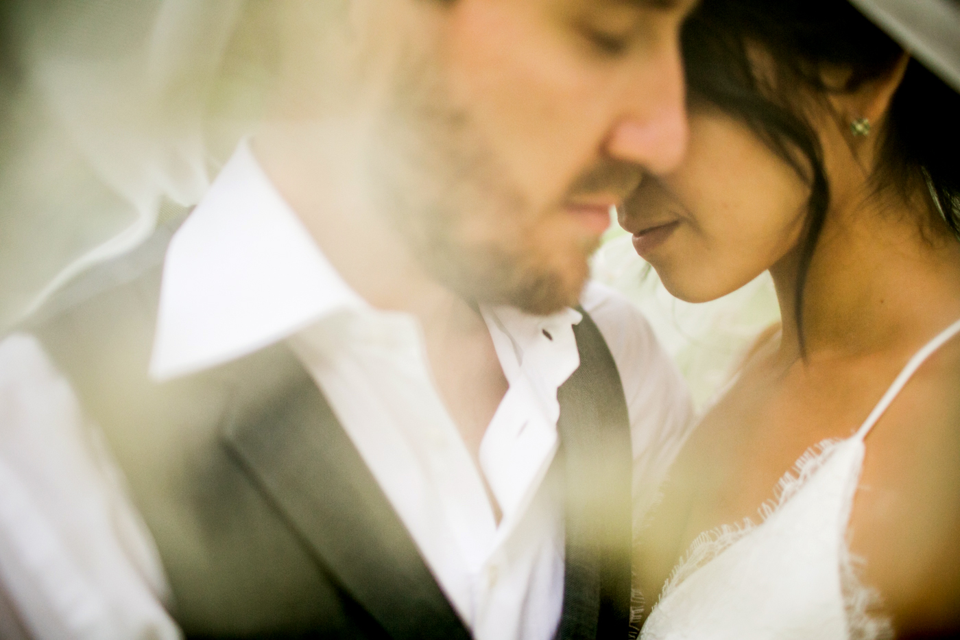 A close-up, softly focused image of a couple gently embracing, their faces touching. The woman wears a white dress and the man wears a white shirt with a dark vest. The overall mood is intimate and romantic. Jessica Hill Photography - Wedding Photographer - Oregon
