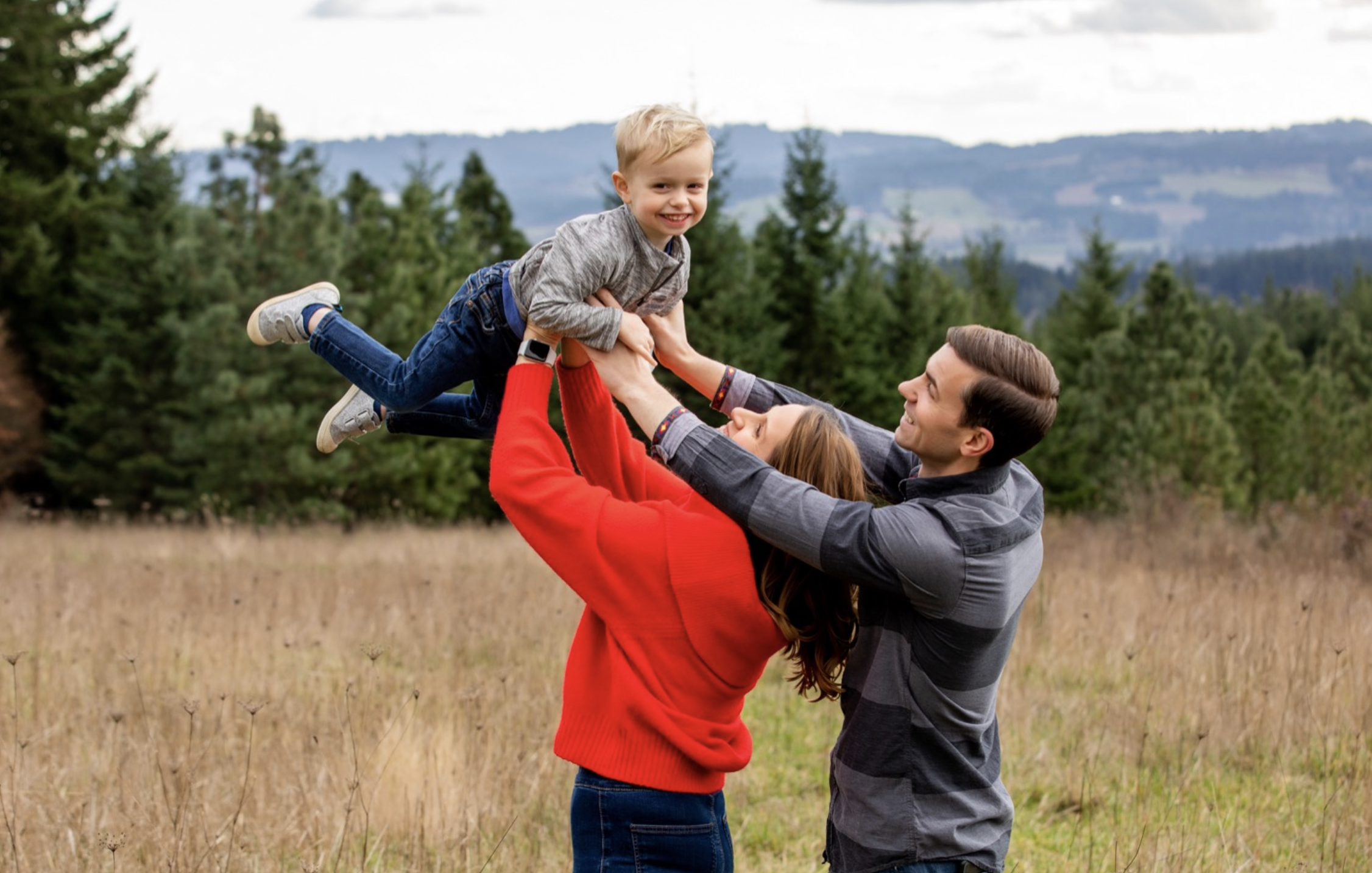 Family lifting child outdoors, forest background.