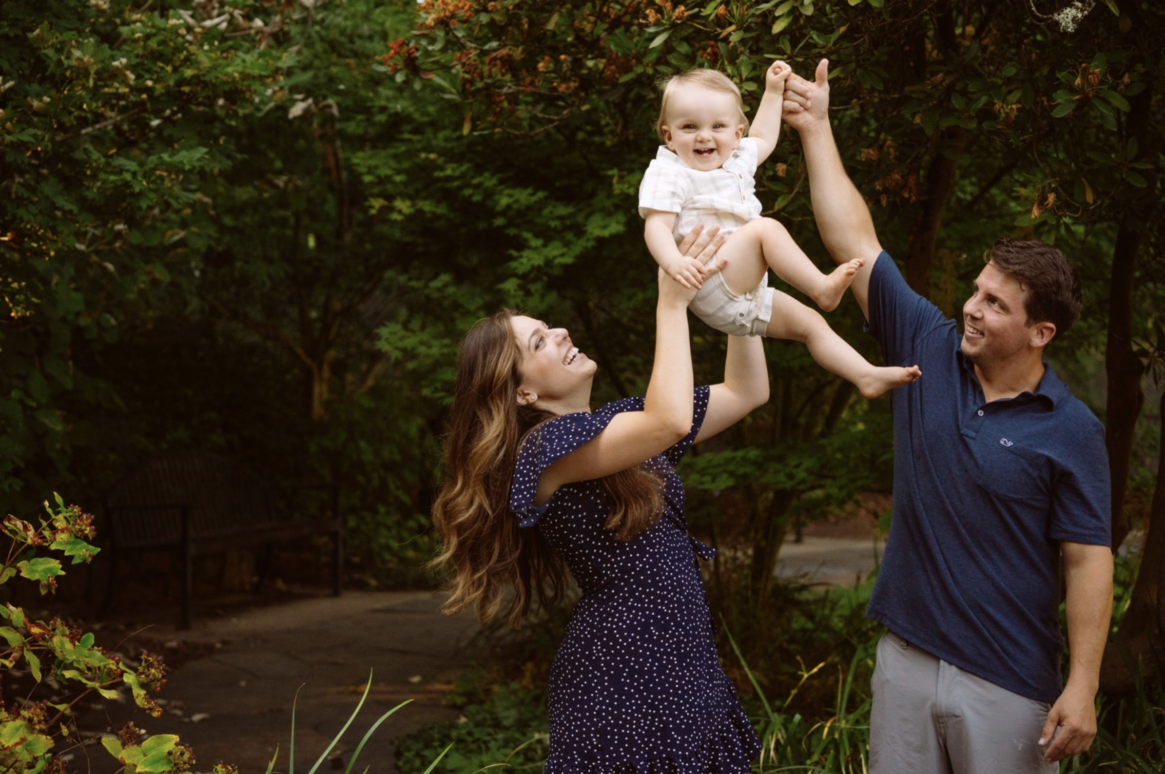 Family joyfully lifting child in garden setting.