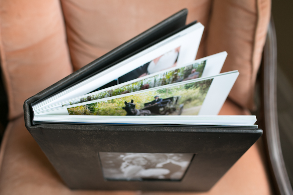 A photo album with a black cover is open on a cushioned chair, displaying several colorful photographs inside. Jessica Hill Photography - Wedding Photographer - Oregon