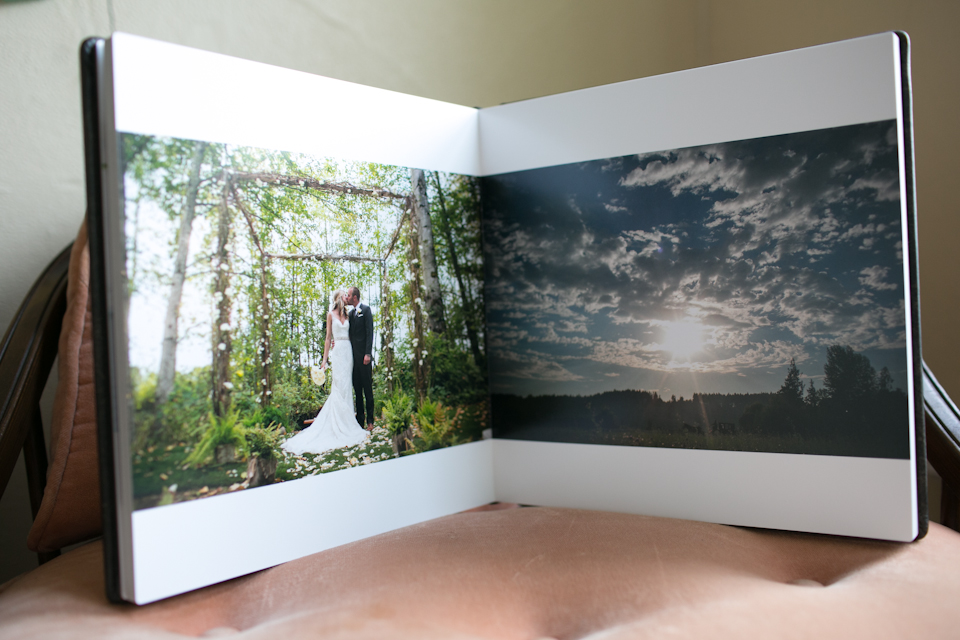 An open photo album on a chair displays a wedding couple standing in a forest on one page and a scenic sky with clouds on the other page. Jessica Hill Photography - Wedding Photographer - Oregon