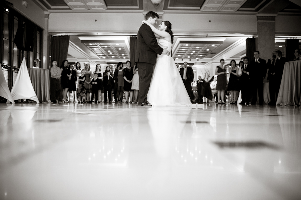 A bride and groom share their first dance in a ballroom as guests stand and watch in the background. Jessica Hill Photography - Wedding Photographer - Oregon