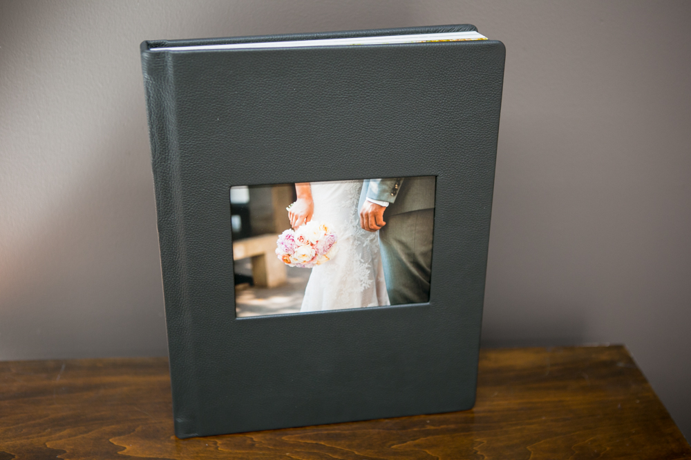 A black photo album with a cover window showing a close-up of a bride and groom holding hands and a bouquet. Jessica Hill Photography - Wedding Photographer - Oregon