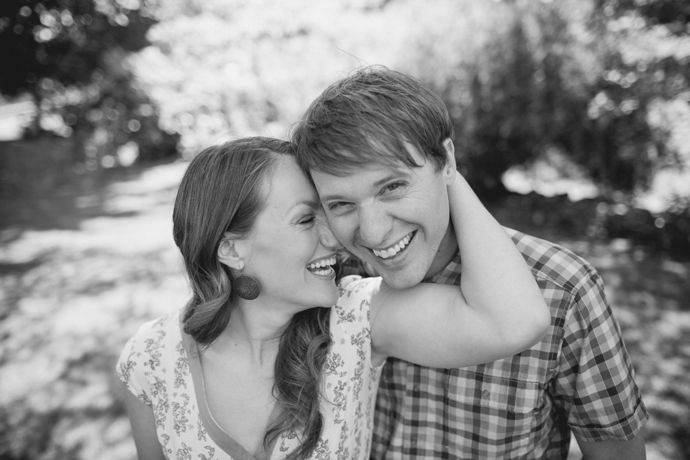 A woman with her arm around a man's neck leans in and smiles while the man also smiles, both outdoors in natural light. Jessica Hill Photography - Wedding Photographer - Oregon