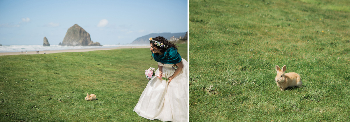 A bride in a white dress stands on a grassy field near the beach, smiling at a small tan rabbit sitting on the grass. In the background, there is a large rock formation by the sea. Jessica Hill Photography - Wedding Photographer - Oregon