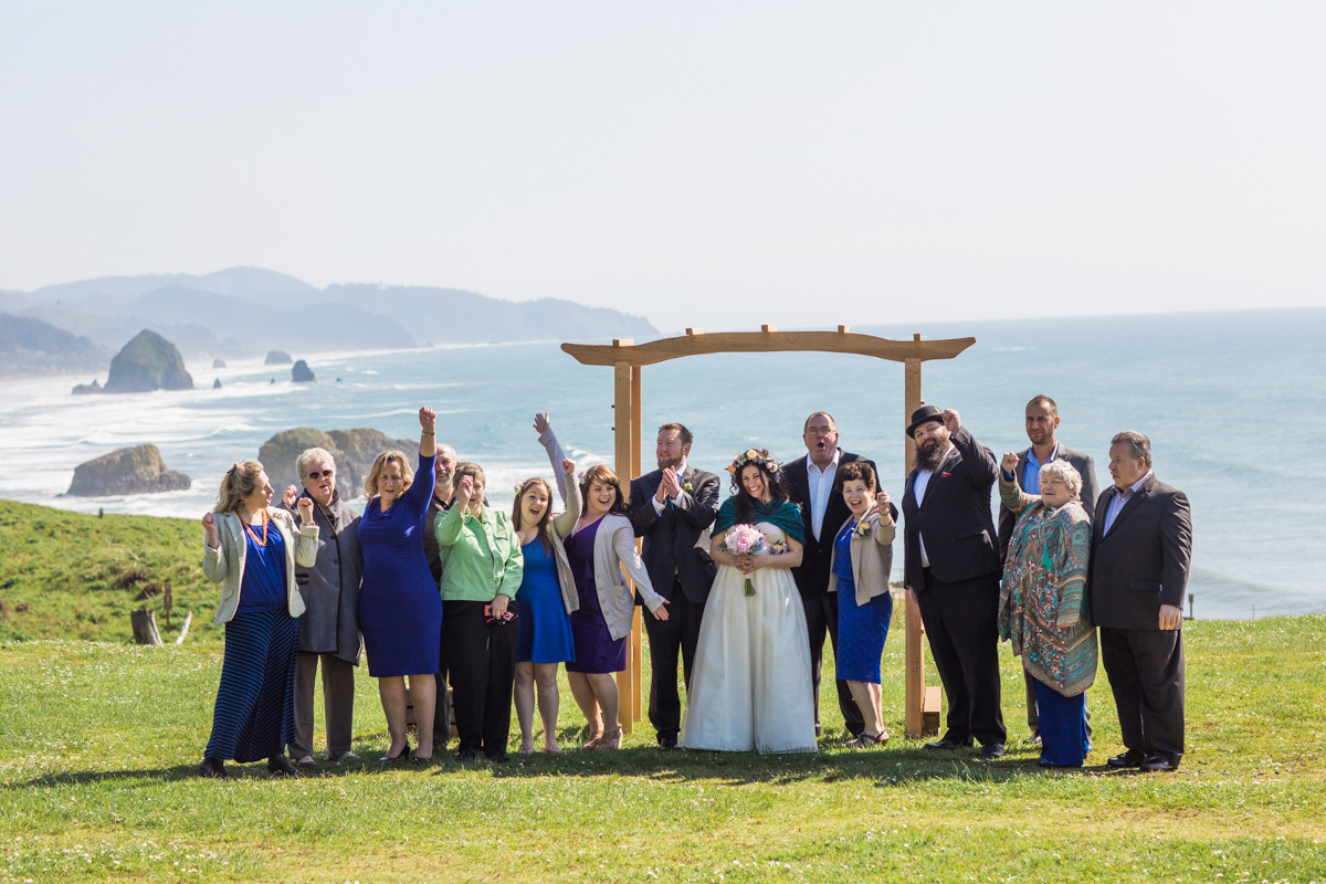 A couple, dressed in wedding attire, runs hand in hand along a sandy beach with tire tracks at sunset, with the ocean and cloudy sky in the background. Jessica Hill Photography - Wedding Photographer - Oregon