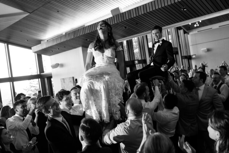 Wedding guests lifting bride and groom on chairs.