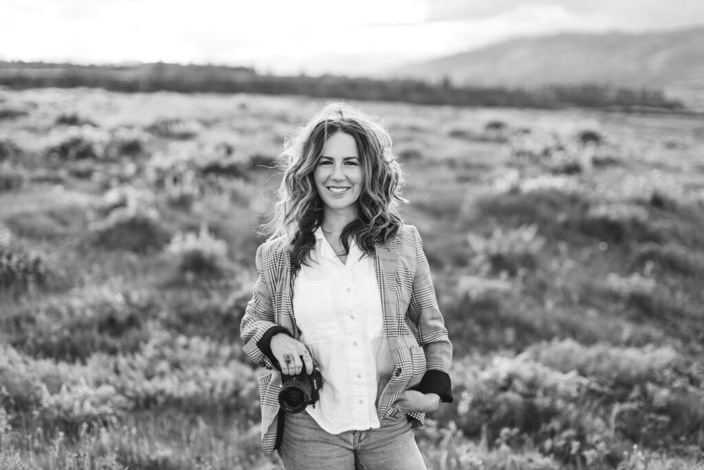 Smiling person holding camera in grass field.