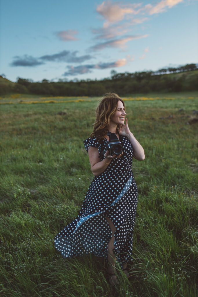 Woman in polka dot dress holding camera in field