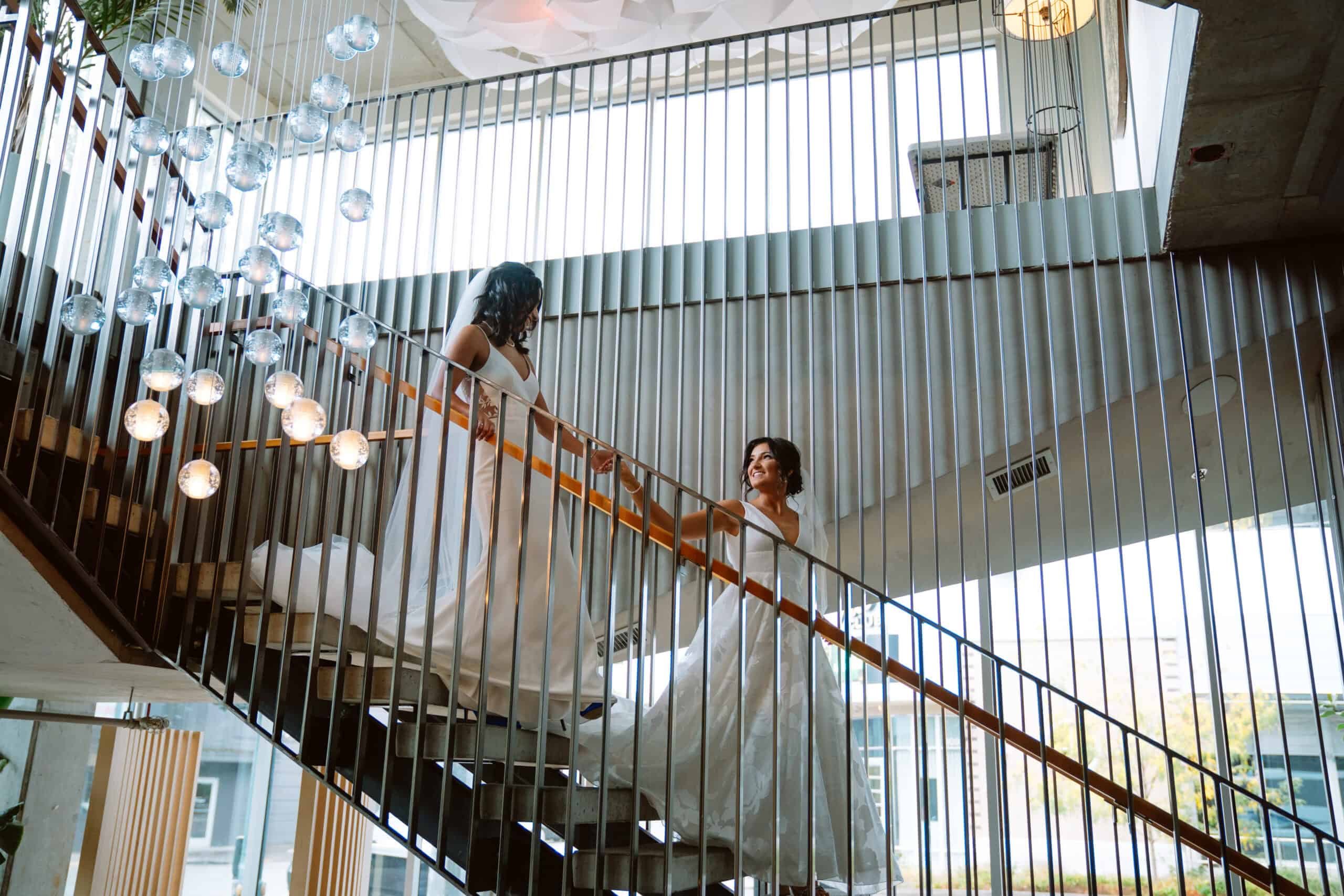 Brides in white dresses on a modern staircase.