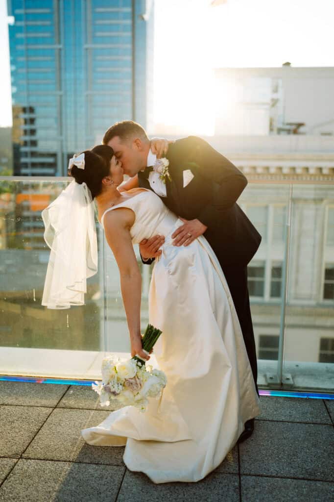 Bride and groom kissing on rooftop at sunset.