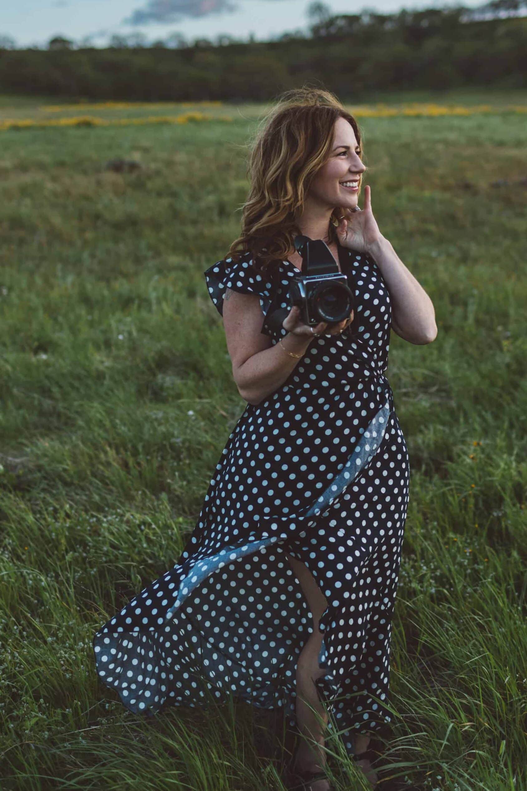 Woman in polka dot dress holding camera in field