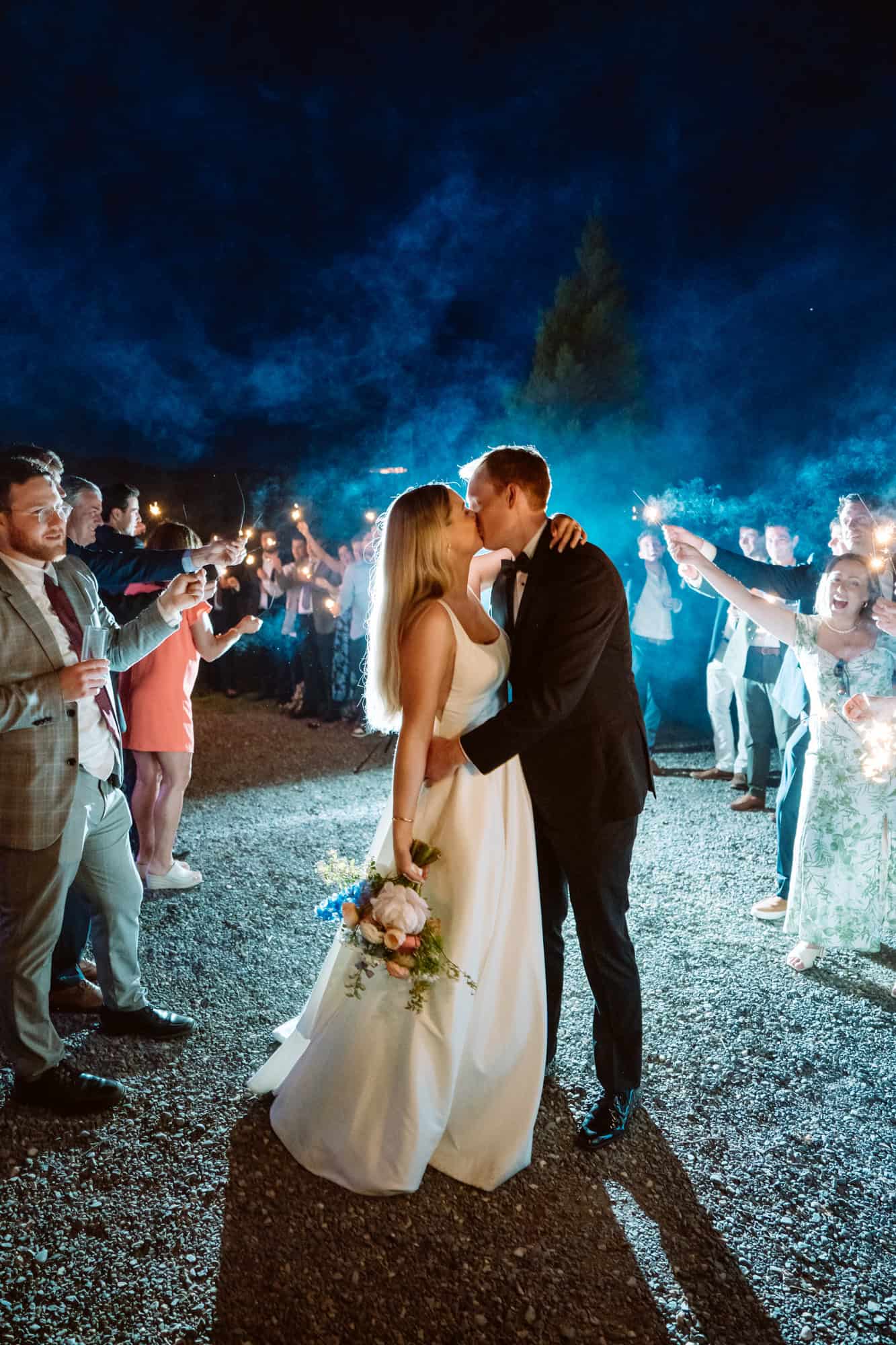 Bride and groom kiss amidst sparklers at wedding night.
