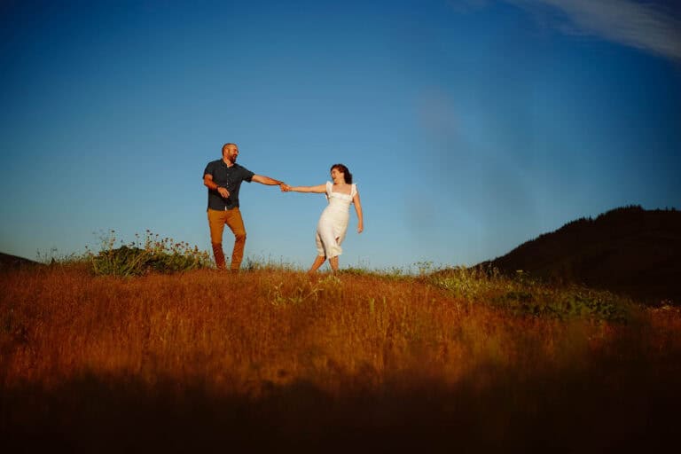 Couple holding hands in scenic field at sunset.
