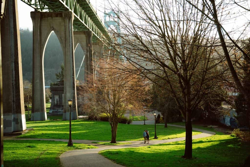 People walking under bridge in sunlit park.