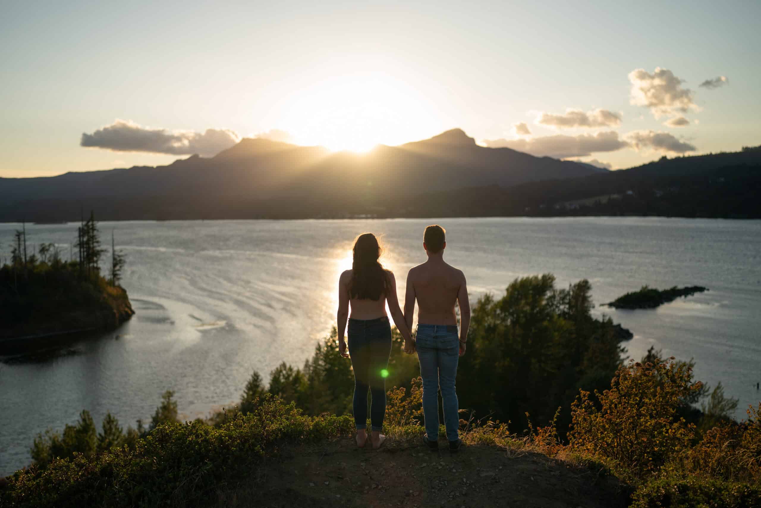 Couple holding hands, overlooking scenic sunset lake view.